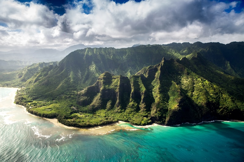 Aerial view of Kauai coastline with lush green mountains meeting the ocean